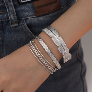 Layered silver feather cuff and chain bracelet set styled on denim background