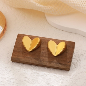 Macro shot of 18K gold heart-shaped stud earrings with cubic zirconia on wooden base