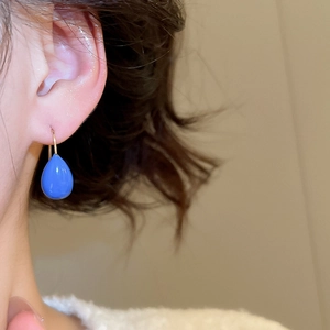 Gros plan d'une boucle d'oreille goutte bleu vif avec crochet doré sur un mannequin