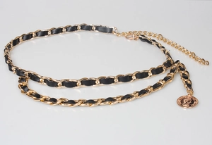 Close-up of gold chain belt woven with black leather and a vintage coin pendant detail