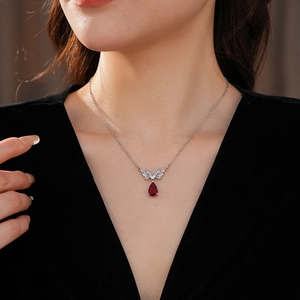 Close-up of a silver necklace featuring a red teardrop pendant and zircon flower details