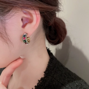 Detailed shot of gold C-shaped earrings with colorful gemstones and crystals on model