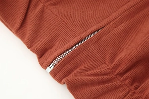 Makroaufnahme von rostrotem Rippstrickgewebe und Silber-Reißverschluss an einem Lounge-Set