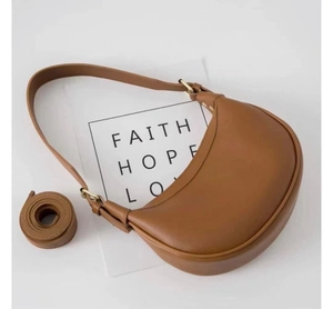 Detail view of a brown crescent saddle bag with two straps and golden hardware