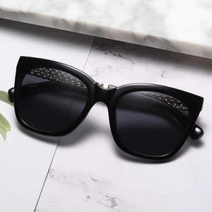 Oversize cat eye sunglasses with gold metal chain trim on black frame, 45-degree angle view