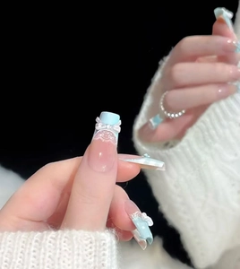 Détail d'ongles longs cercueil avec dentelle bleue, nœuds et perles sur fond doux