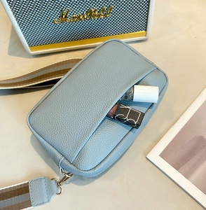 Close-up of light blue lychee pattern leather bag with a wide striped shoulder strap