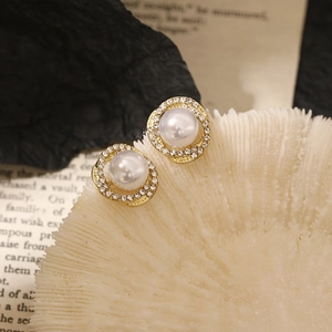 Detailed close-up of golden spiral pearl earrings with rhinestones on white coral decor