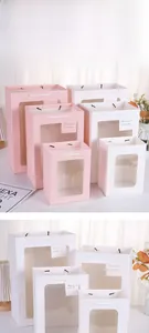 Détail de sacs cadeaux en papier avec fenêtre transparente, anses blanches et étiquettes