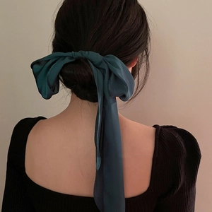 Deep green silk ribbon hair tie styled in a large bow on a classic bun hairstyle