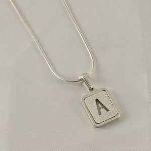 Macro detail of silver rectangular pendant with frosted texture and hollow letter A