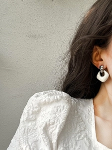 Close-up of geometric white enamel earring with silver metal top on a female model