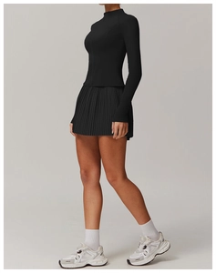 Side view of woman in black slim-fit zip jacket and pleated sports skirt with white shoes