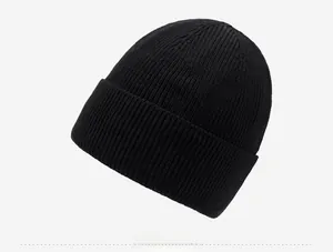 Close-up of black knitted beanie featuring fine ribbing and a circular metal logo detail