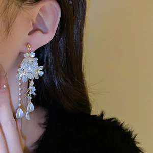 Gros plan de boucles d'oreilles fleurs avec pétales blancs et franges dorées sur mannequin