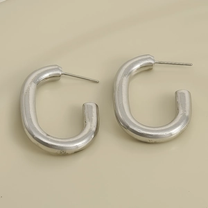 Close-up of a pair of silver C-shaped 304 stainless steel earrings on a beige surface