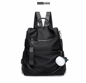 Detailed close-up of a black nylon backpack featuring a white pompom and metal rivet strap