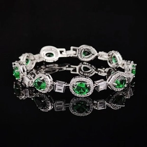 Macro shot of silver bracelet with emerald green zircons and white diamond accents on black base
