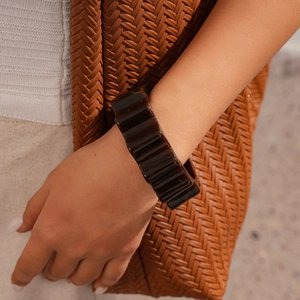 Detail of chunky acrylic wave bangle in tortoiseshell brown resin on a model's wrist