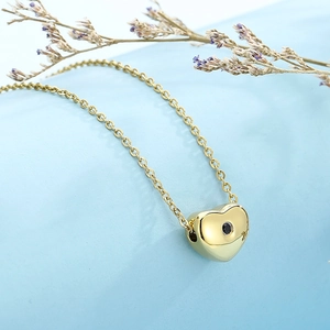 Detail of a golden heart necklace with black stone on a soft light blue background