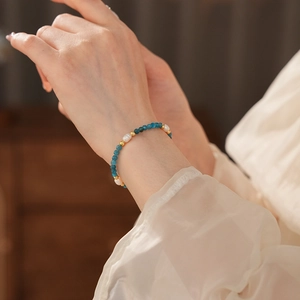 Elegant beaded bracelet with blue stones, white pearls and gold accents on a model wrist