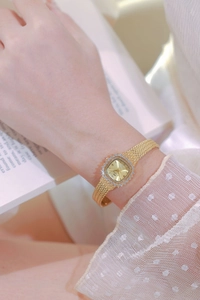 Elegant gold square watch with crystal-encrusted bezel and mesh band on female wrist