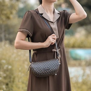 Classic dark brown printed saddle bag with adjustable strap worn by model in outdoor setting