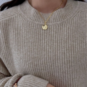 Close-up of golden coin pendant necklace with hammered texture on a beige knit sweater