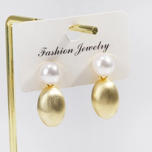 Detail of white pearl stud earrings with brushed gold oval pendant on display card