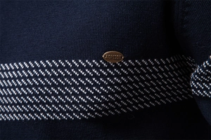 Dettaglio macro del tessuto a maglia blu scuro con trama geometrica e logo in metallo