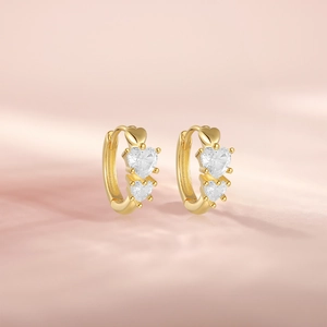 Detail of golden hoop earrings with heart-shaped cubic zirconia on a pink background