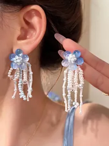 Detail of flower tassel earrings featuring blue petals and white beaded fringes on a model