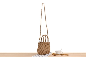 Close-up of light brown woven paper straw bag on wooden table with dried wheat and tea cup