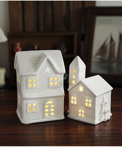 Close-up of two white ceramic lighted Christmas houses on a rustic wooden table surface