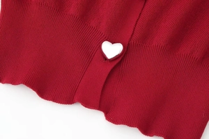 Detail of red knit cardigan featuring a heart-shaped silver metal button close-up