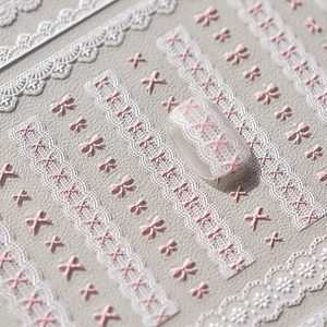 Macro shot of 3D embossed nail art stickers featuring white lace and pink bow designs