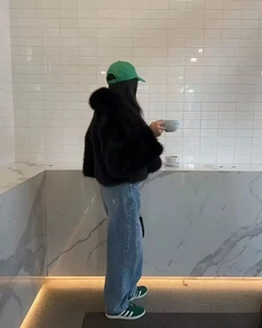 Vue latérale d'une veste courte noire en fausse fourrure pelucheuse avec un jean décontracté