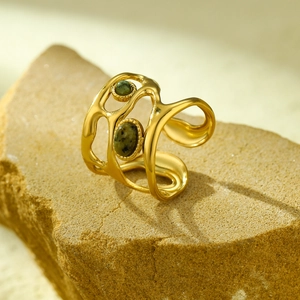Detail of gold open ring with irregular hollow frame and green oval gemstones on a stone