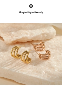 Detailed view of layered C-shaped earrings in gold and rose gold on a natural stone base