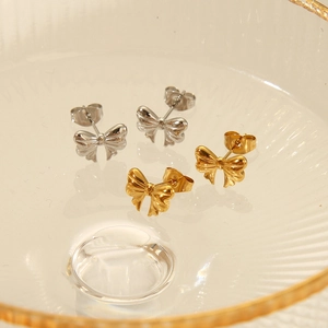 Elegant bow-knot earrings in gold and silver finish on a textured glass tray