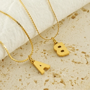 Gold plated stainless steel letter A and B pendant necklaces on a stone surface