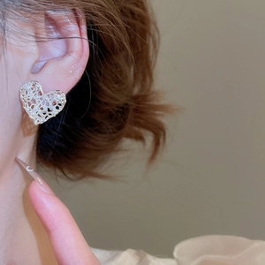 Macro detail of silver heart stud earrings with intricate openwork lace metal texture