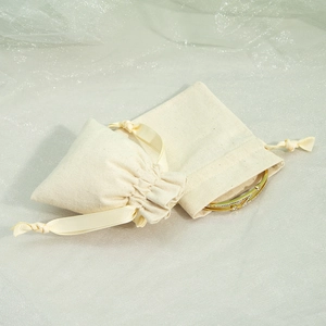 Close-up of beige cotton jewelry drawstring bags with a gold bracelet detail