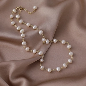 Detalle de collar de perlas de agua dulce con cadena de corazón en fondo de seda