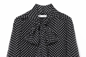 Detail view of polka dot chiffon shirt neckline with elegant bow-tie and brand label