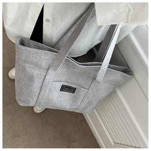 Detailed close-up of gray woven tote bag fabric texture held by a model in casual setting