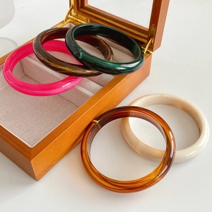Detail of colorful resin bangles in tortoise, marble and amber tones on a wood box