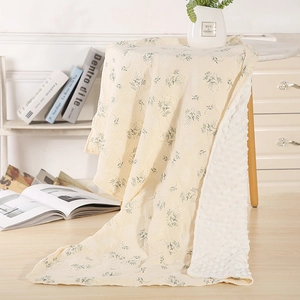 Macro detail of a double-sided baby blanket featuring floral gauze and soft minky dot texture