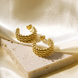 Close-up of golden hollow twisted texture hoop earrings on a beige stone surface