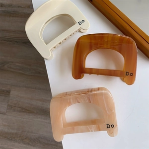 Three acetate hair claws in beige, amber and pink marble finish with 'Do' lettering